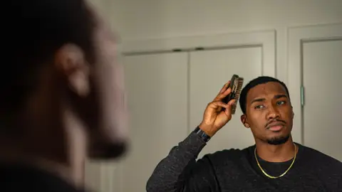 A young man looks at his reflection while getting ready in front of a mirror.